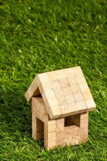 Symbolhaus auf Rasenfläche ein Holzhaus aus Bauklötzen auf einer Rasenfläche