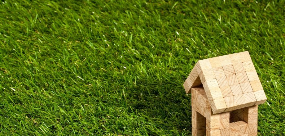 Symbolhaus auf Rasenfläche ein Holzhaus aus Bauklötzen auf einer Rasenfläche
