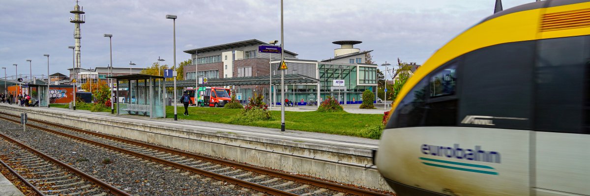 Hier ist der Warendorfer Bahnhof mit einem hereinfahrenden Zug sowie Bussen im Hintergrund abgebildet.