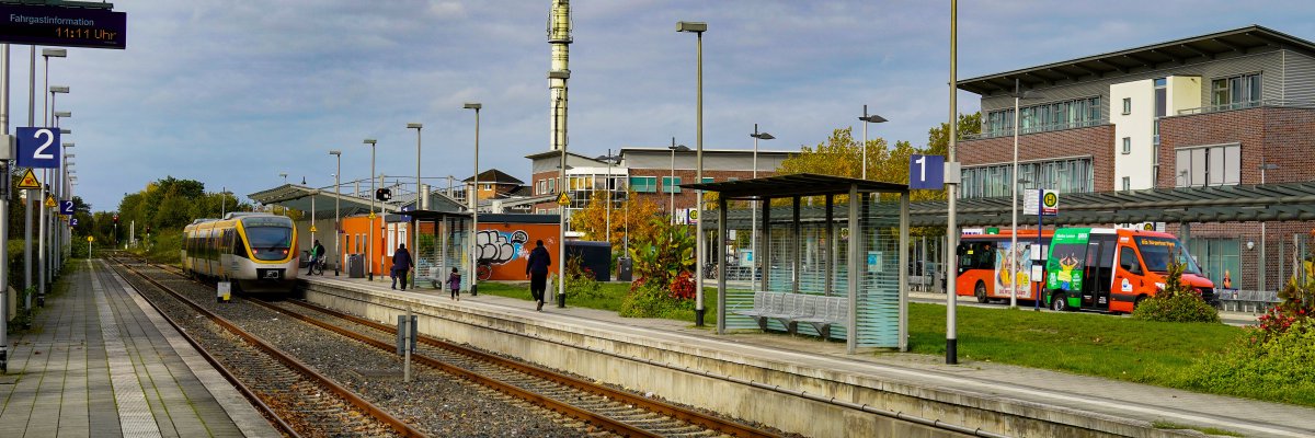 Hier ist der Warendorfer Bahnhof mit einem hereinfahrenden Zug sowie Bussen im Hintergrund abgebildet.