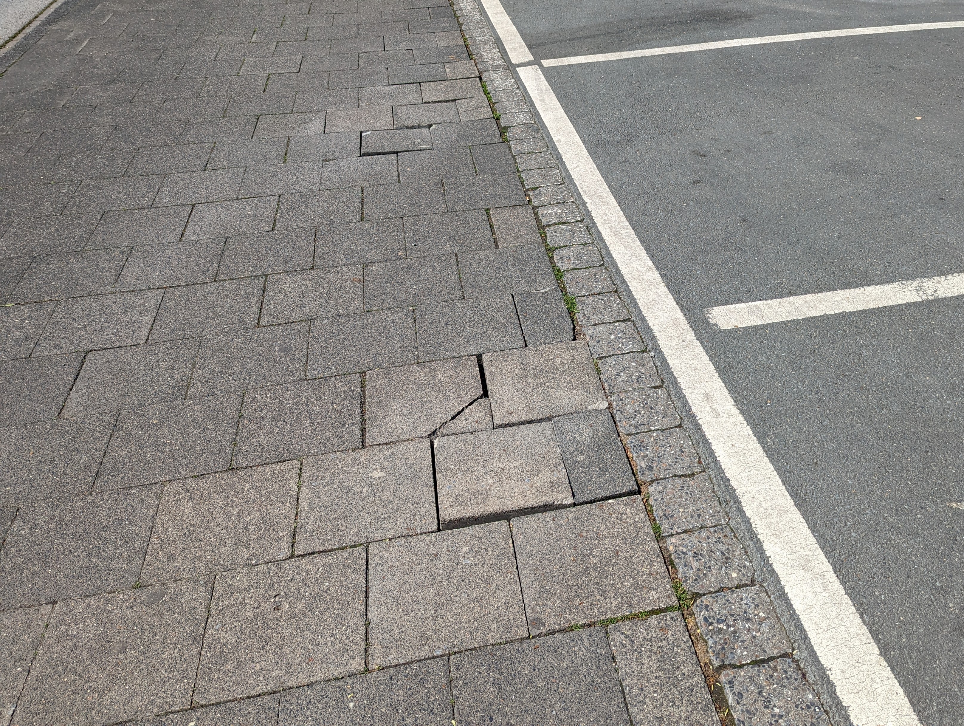 Beschädigte Gehwegplatten mit fehlender Bettung.