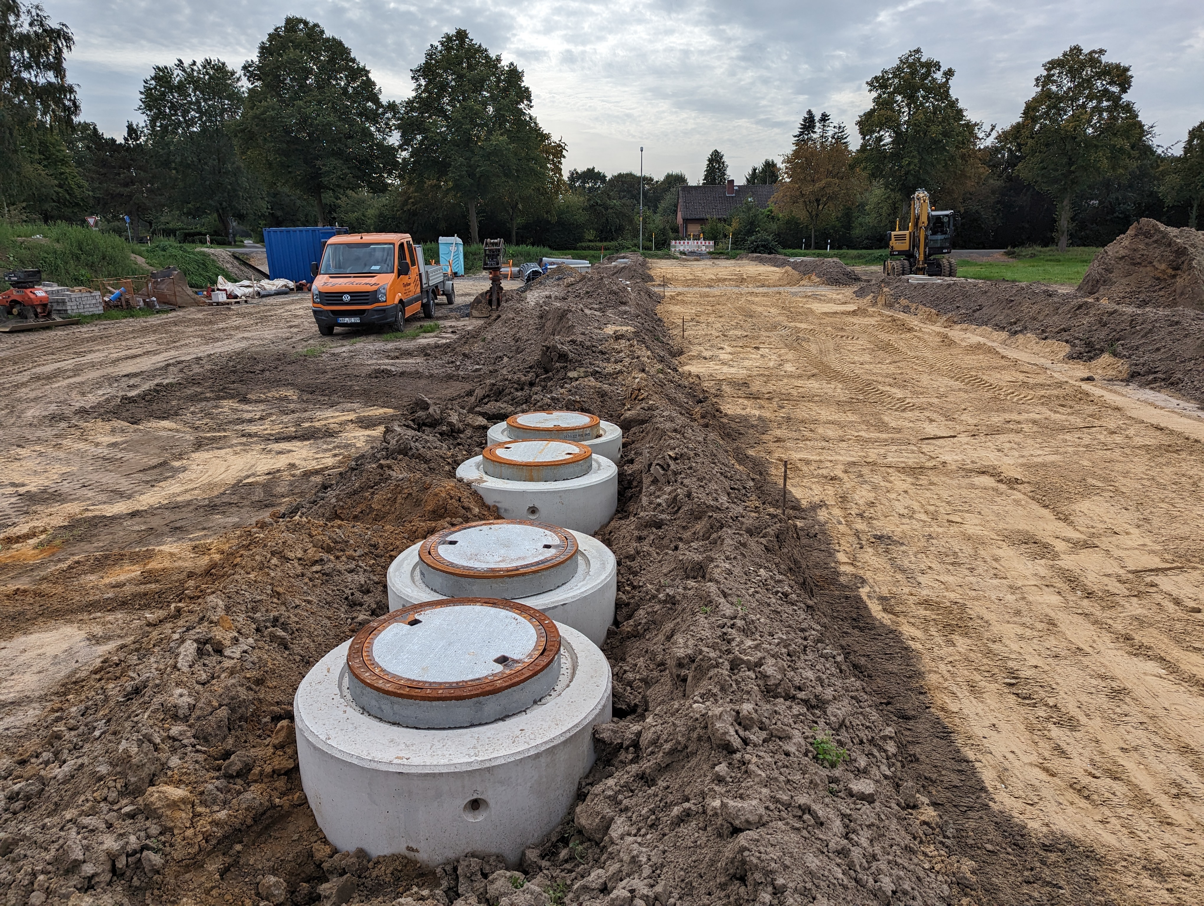 Ein Feld auf dem  Erdarbeiten stattfinden. Im Fokus sind mehrere Schächte, die noch nicht bis zur Krone angefüllt sind. Im Hintergrund sind Baustellenfahrzeuge zu erkennen.