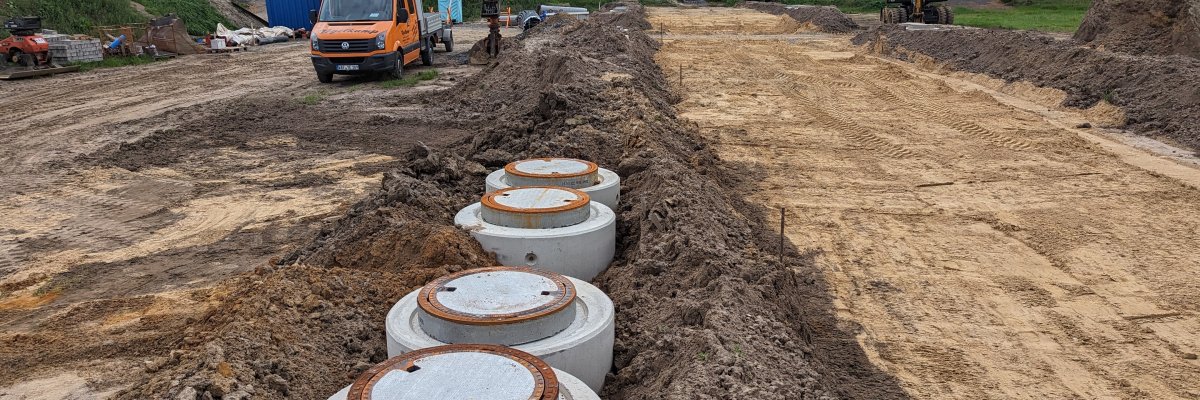 Ein Feld auf dem  Erdarbeiten stattfinden. Im Fokus sind mehrere Schächte, die noch nicht bis zur Krone angefüllt sind. Im Hintergrund sind Baustellenfahrzeuge zu erkennen.