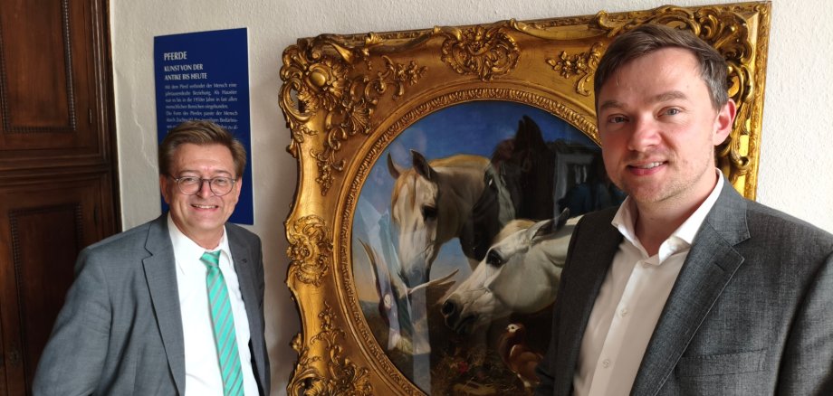 Zwei Männer vor einem Bild mit Pferden und Tauben
