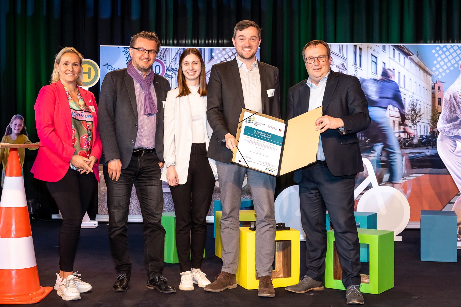 Das Bild zeigt die Urkundenübergabe zur Mitgliedschaft Warendorfs zum Zukunftsnetz Mobilität NRW. Auf dem Foto sind von rechts nach links: NRW-Verkehrsminister Oliver Krischer, Bürgermeister Peter Horstmann, Mobilitätsmanagerin Lea Licher, NWL-Geschäftsführer Joachim Künzel und Daniela Niestroy-Althaus vom Zukunftsnetz Mobilität NRW.